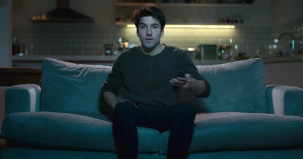 Man sits down on a sofa, switches on the tv using a remote control. - Felvétel, videó