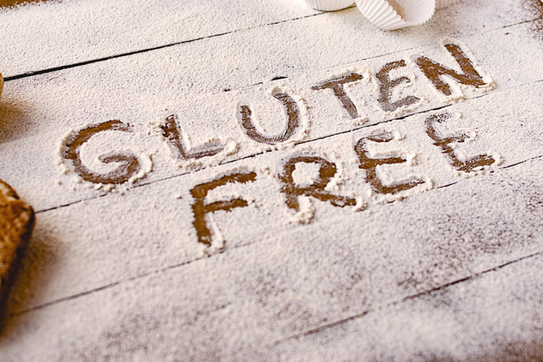 Gluten free concept. Wooden table with flour and pastry material, with the written phrase gluten free. - Фото, изображение