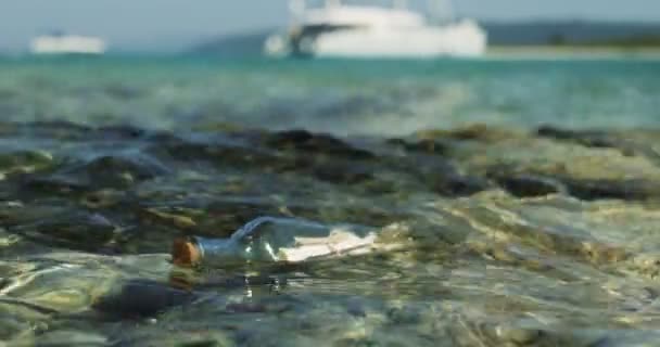 Close-up Shot vzkaz v láhvi, driftování v mělkých mořích s bílé jachty na pozadí. - Záběry, video
