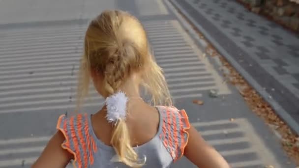 Small beautiful girl walks along tall fence, lit by sun. - Footage, Video