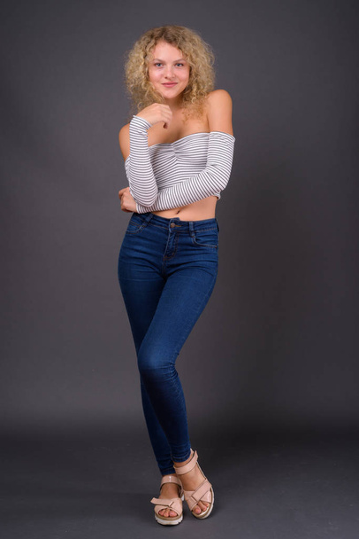 Young beautiful woman with blond curly hair against gray backgro - Foto, afbeelding
