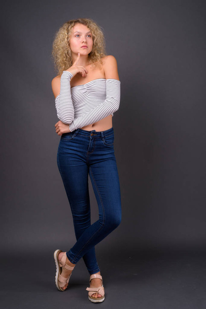 Studio shot of young beautiful woman with blond curly hair against gray background - Zdjęcie, obraz