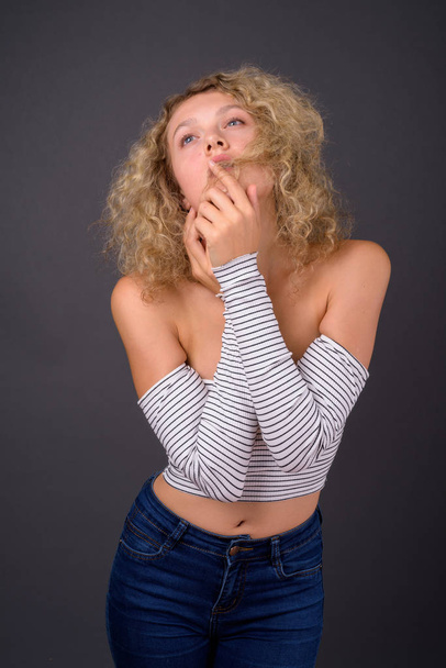 junge schöne Frau mit blonden lockigen Haaren gegen grauen Backgro - Foto, Bild