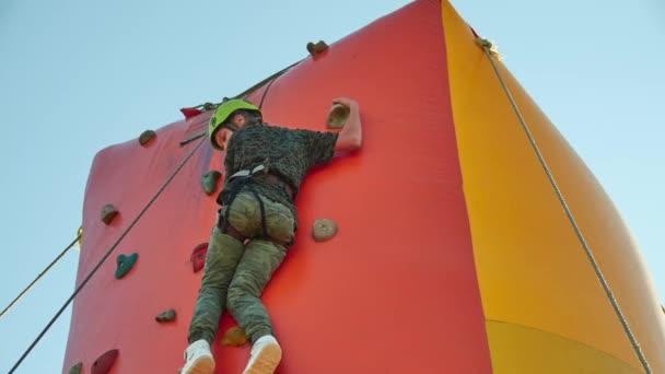 Girl in helmet climbs on Climbing wall. Climbing wall is an artificially constructed wall with grips for hands and feet. - Footage, Video
