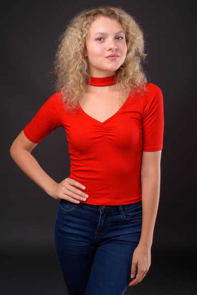 Молодая красивая женщина с кудрявыми светлыми волосами против серого бэкгро
 - Фото, изображение