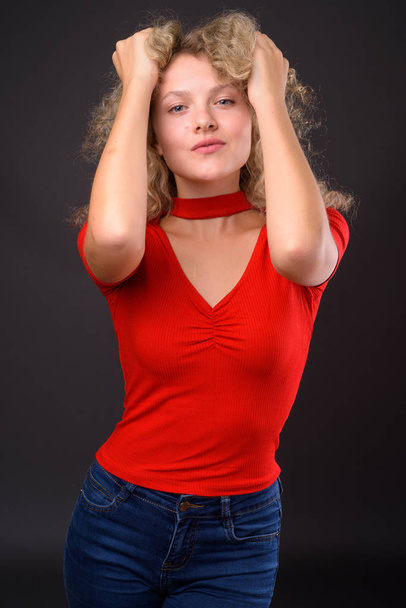 Νεαρή όμορφη γυναίκα με ξανθά σγουρά μαλλιά ενάντια σε γκρι backgro - Φωτογραφία, εικόνα