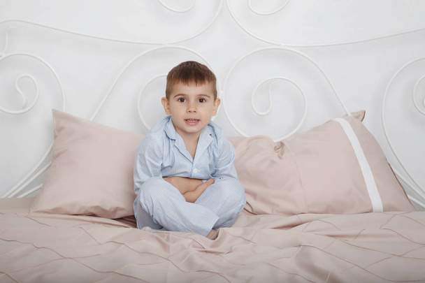 Mały chłopiec w niebieskim piżamy wali w łóżku pościel i poduszki. - Zdjęcie, obraz