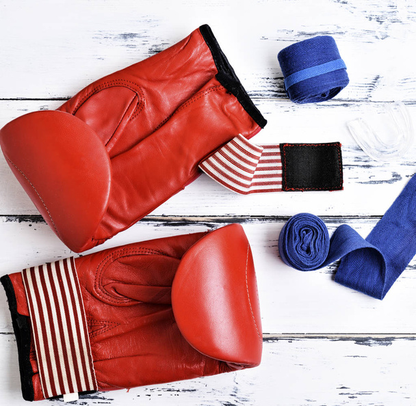 paire de gants de boxe en cuir rouge, bandage bleu et embout buccal en silicone sur fond bois blanc, vue de dessus
 - Photo, image
