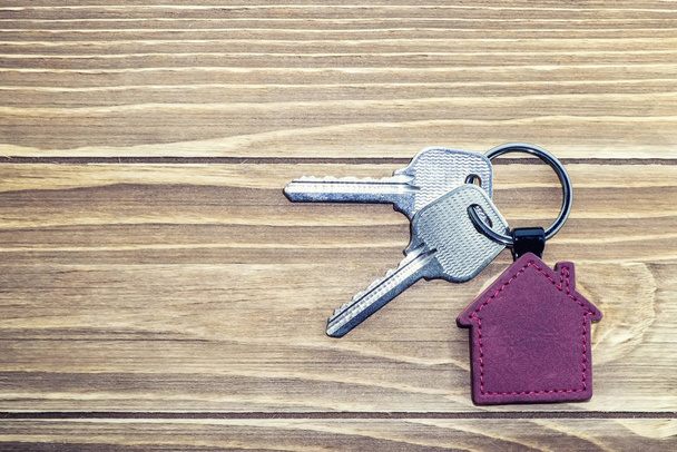 Schlüsselanhänger mit Haussymbol und Schlüsseln auf Holzgrund, Immobilienkonzept - Foto, Bild