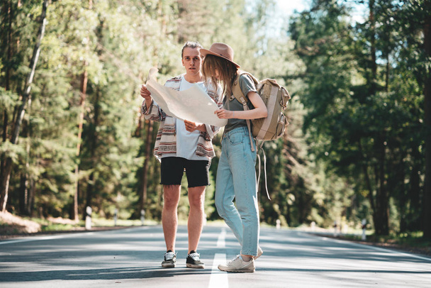 Young hipster couple travelers looking on the location map. Adult man and girl traveling together on forest road - Foto, Imagen