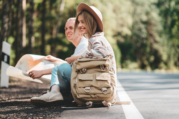 Couple travelers woman and man sitting on road and looking forward to a joint journey. Lifestyle concept. Young happy family traveling adventure vacations - Foto, immagini