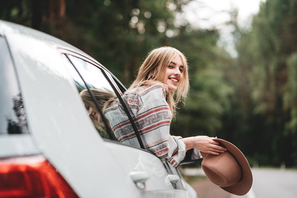 Boho style woman is sitting at the wheel of a car and look into the great distance. Pretty girl hipster enjoying forest road - Foto, Imagem