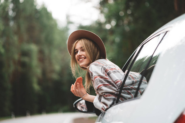 Pretty and style woman traveler sitting in car and looking from window on wild road. Boho girl, wanderlust. Wearing checkered shirt - Foto, Imagem