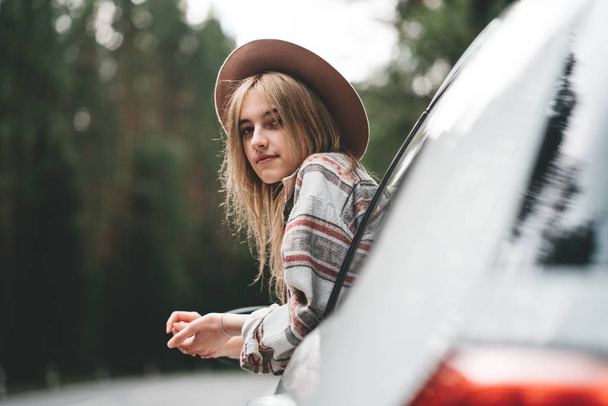 Handsome woman sitting in car looking from window on beautiful view in forest. Pretty girl hipster enjoying country road. Lifestyle concept - Foto, immagini
