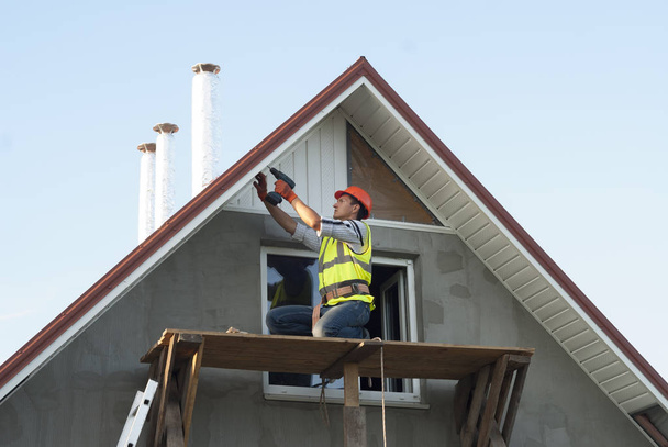 建設労働者は屋根庇の軒裏をマウントします。 - 写真・画像