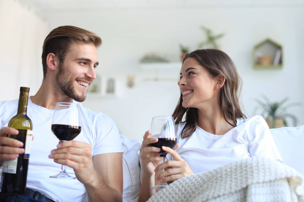 Young loving couple drinking a glass of red wine in their living room. - Fotografie, Obrázek