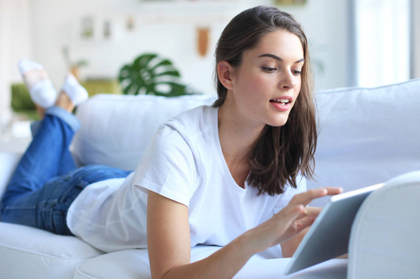 Beautiful young woman using tablet sitting on sofa at home at living room. - Foto, Bild