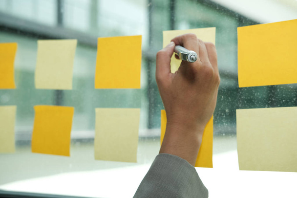 Empresario escribir en notas adhesivas en la pared de vidrio en el lugar de trabajo. Programa de recordatorio de papel pegajoso para discutir ideas creativas y lluvia de ideas de negocios
 - Foto, Imagen