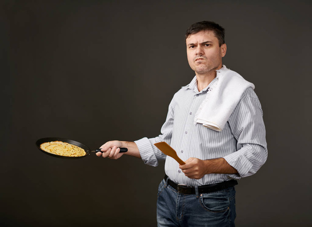 man posing with a pancake in a pan, white shirt and pants, gray background, surprised emotions - Photo, Image