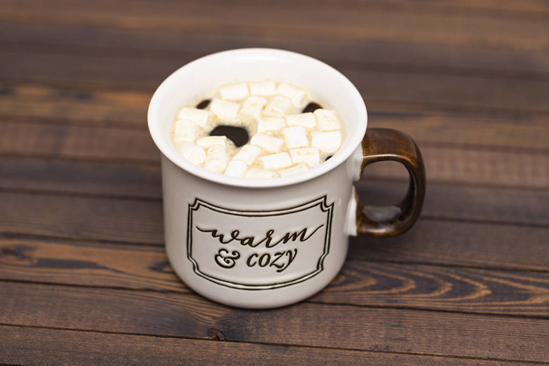 Cocoa with marshmallows on a wooden background in a Cup with the inscription " Warm and cozy" - Foto, afbeelding
