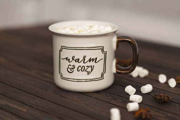 Cocoa with marshmallows on a wooden background in a Cup with the inscription " Warm and cozy" - Foto, Imagen
