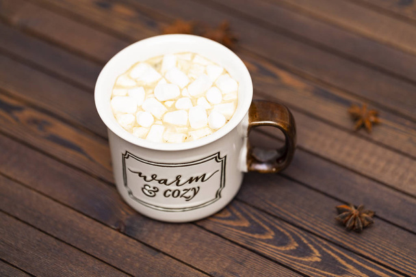 Cocoa with marshmallows on a wooden background in a Cup with the inscription " Warm and cozy" - Valokuva, kuva