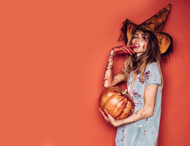 Halloween girl with a carved Pumpkin. Beautiful young surprised woman in costume holding pumpkin. Halloween Witch with pumpkin. Sexy vampire woman with blood on her face. Halloween party art design. - Foto, immagini