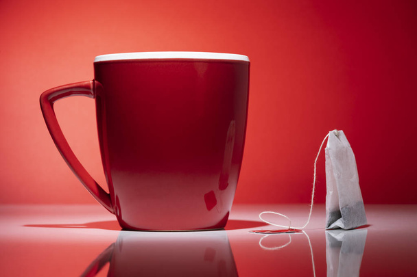 Piros bögre és egy teafiltert, elszigetelt a piros háttér - Fotó, kép
