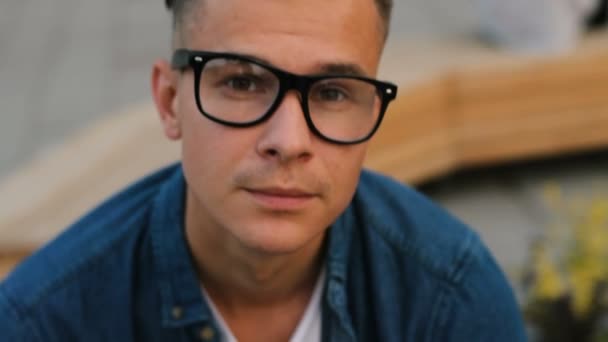 Portrait of young handsome man in the glasses looking to the camera and smiling on the city background. Close up shot. - Filmati, video
