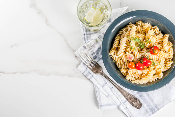 Classic italian pasta fusilli with pesto sauce, tomatoes, lime and fresh herbs in dark bowl, white marble background  copy space above - Фото, изображение