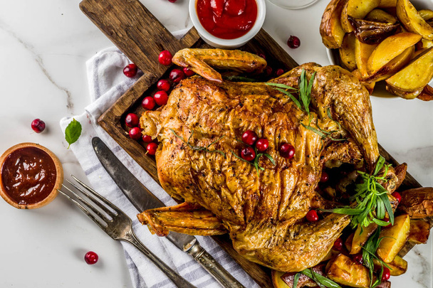 Χριστούγεννα, ημέρα των Ευχαριστιών τροφίμων, ψημένο κοτόπουλο ψητό με κράνμπερι και βότανα, σερβιρισμένο με τηγανητά λαχανικά, φρέσκα μούρα κρασιού και σάλτσες σε λευκό μαρμάρινο τραπέζι, αντιγράψτε κάτοψη χώρου - Φωτογραφία, εικόνα