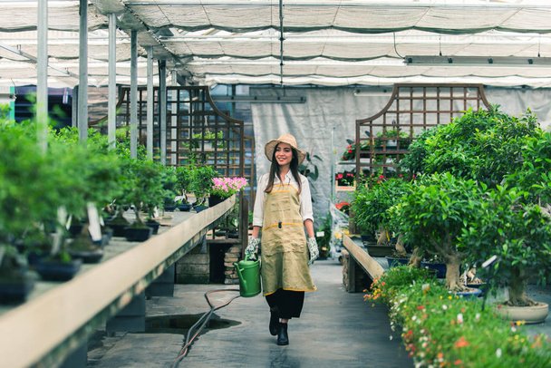 Pretty female gardener taking care of plants in her flowers and plants shop - Asian woman working in a greenhouse - Photo, Image