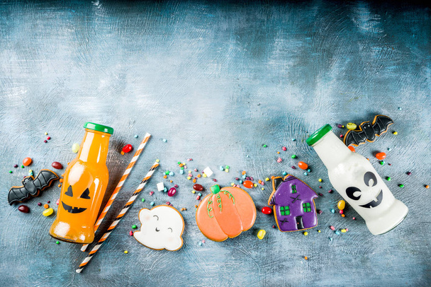 dolcetti per bambini per Halloween, biscotti smaltati fatti in casa divertenti, varie caramelle latte e succo in bottiglia mostro, sfondo di cemento blu copia spazio vista dall'alto
 - Foto, immagini