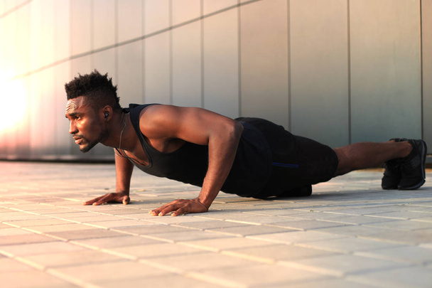 African man in sports clothing keeping plank position while exercising outdoors. - Φωτογραφία, εικόνα