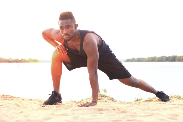 African man in sports clothing warming up, in beach outdoor portrait, at sunset or sunrise. - Photo, Image