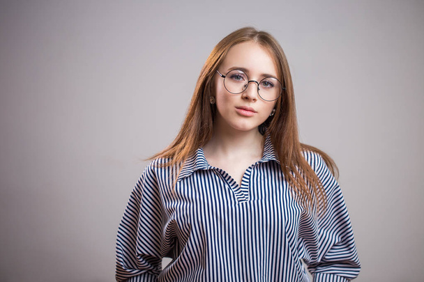Horizontal portrait of beautiful young woman wearing glasses and shirt on grey background. Student girl looking at camera - Foto, afbeelding