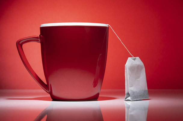 Červený hrnek a sáček čaje, izolované na červeném pozadí - Fotografie, Obrázek