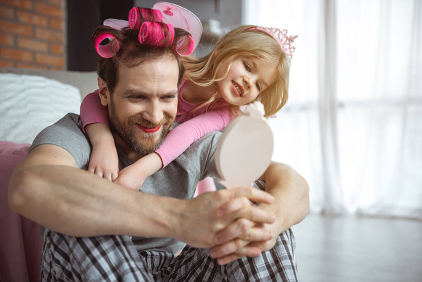 Positive man with facial makeup looking at mirror with daughter  - Zdjęcie, obraz