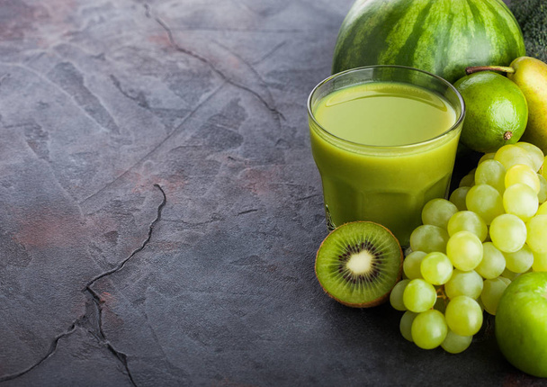 Glass of fresh smoothie with organic green toned fruits on stone kitchen table background. Pear and grapes with kiwi and lime with apple.  - Photo, Image