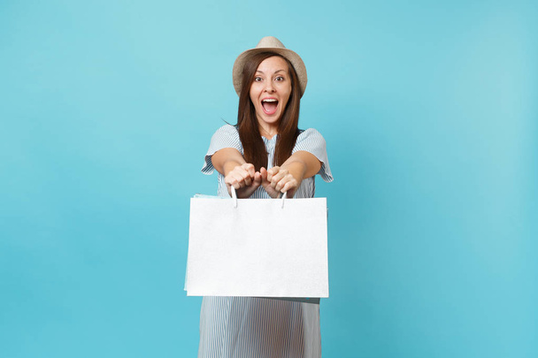 Portrait excité souriant belle femme caucasienne en robe d'été, chapeau de paille tenant paquets sacs avec des achats après les achats isolés sur fond bleu pastel. Espace de copie pour la publicité
 - Photo, image