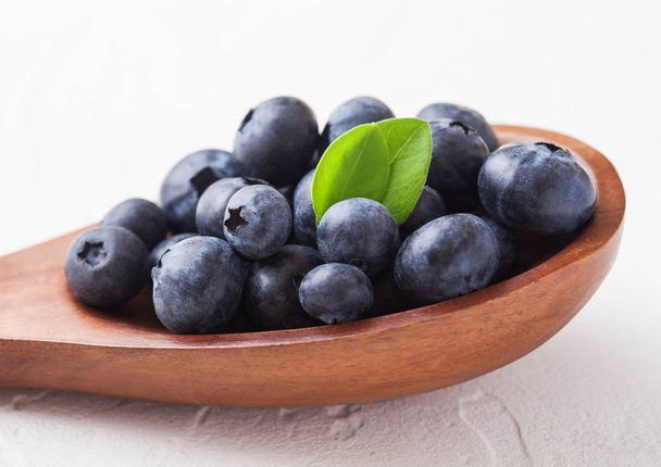 Fresh raw organic blueberries with leaf on wooden spoon on white kitchen background. Food concept. - Photo, image