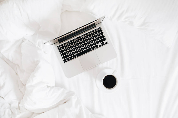 Práce na ranní koncept. Laptop a kávu v posteli na bílým ložním prádlem. Plochá ležel, horní pohled minimalistickém prostoru pozadí. - Fotografie, Obrázek