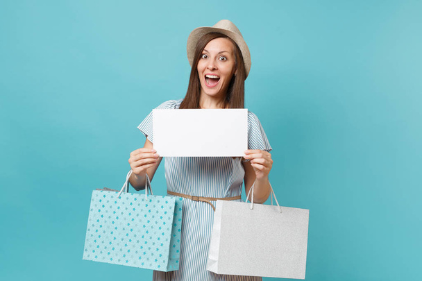Portrait woman in summer dress, straw hat holding packages bags with purchases after shopping, empty blank Say cloud, speech bubble card isolated on blue pastel background. Copy space advertisement. - Fotografie, Obrázek