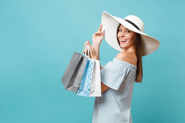 Retrato elegante moda bela mulher caucasiana no vestido de verão, branco grande chapéu de sol de aba larga segurando pacotes sacos com compras depois de fazer compras isoladas em fundo pastel azul
 - Foto, Imagem