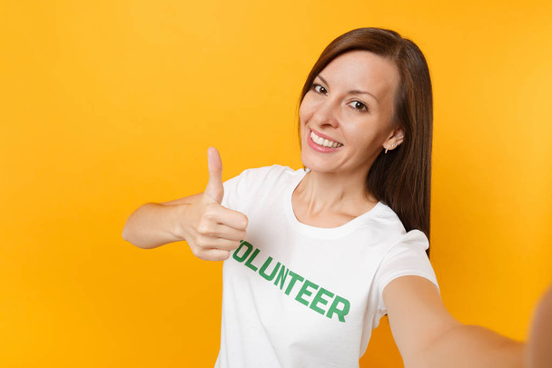 Селфі-зображення щасливої усміхненої задоволеної жінки в білій футболці з написаним написом зелений титул добровольця ізольовано на жовтому фоні. Добровільна безкоштовна допомога, концепція благодійної роботи
 - Фото, зображення