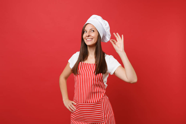 Dona de casa cozinheiro chef ou padeiro em avental listrado t-shirt branca, chapéu de chefs toque isolado no fundo da parede vermelha. Sorrindo mulher bonita calma fazendo bom gosto deleite sinal. Mock up conceito de espaço de cópia
 - Foto, Imagem