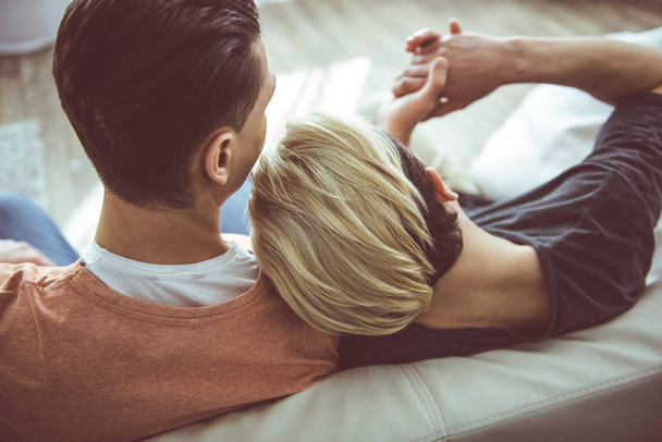 jovem gay casal sentado no sofá e abraço
 - Foto, Imagem