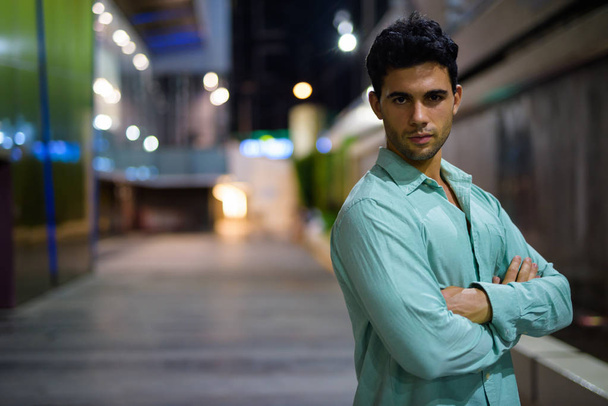 Young handsome Hispanic man exploring the city streets at night - Foto, afbeelding