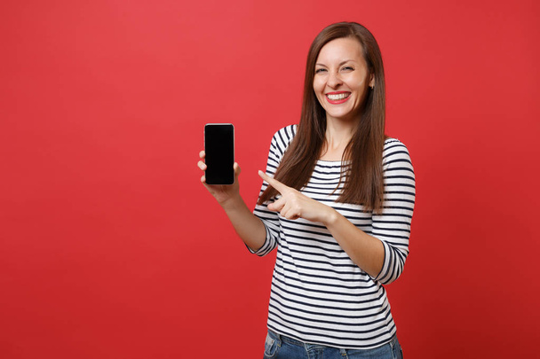 Портрет красивой молодой женщины, указывающей указательным пальцем на мобильный телефон с пустым черным пустым экраном, изолированным на ярко-красном фоне. Люди искренние эмоции, образ жизни концепции. Пространство для копирования
 - Фото, изображение