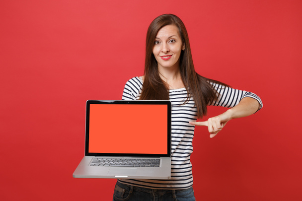 attraktive junge Frau zeigt mit dem Zeigefinger auf Laptop-PC-Computer mit leeren schwarzen leeren Bildschirm isoliert auf leuchtend rotem Wandhintergrund. Menschen aufrichtige Emotionen, Lebensstil-Konzept. Attrappe Kopierraum - Foto, Bild